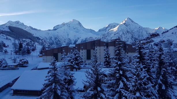 A snow-covered mountain resort with modern buildings, ski slopes, and snow-laden trees. - South expo studio, heart resort, calm, ski to door (Les Deux Alpes)