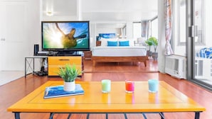Una habitación de hotel con cama, televisión, una mesa de madera con velas y una ventana con cortinas.