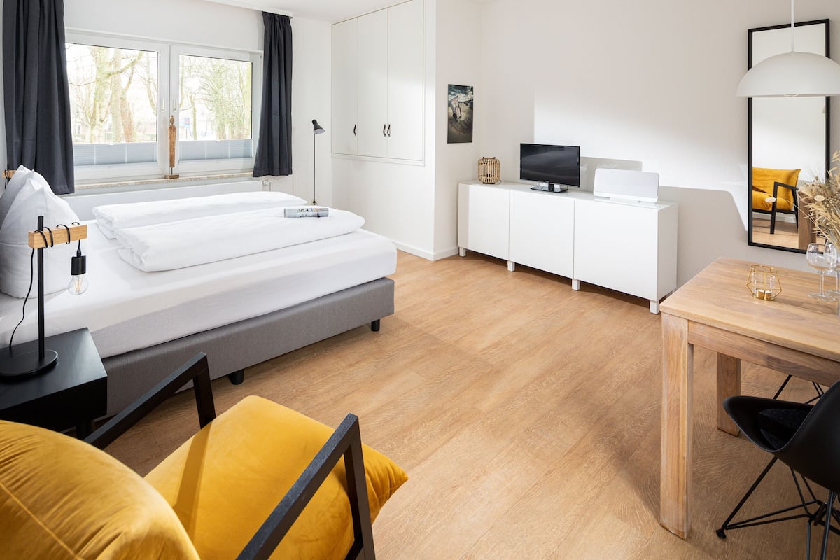 A modern hotel room with a bed, bedside table, lamp, and a desk with a chair.