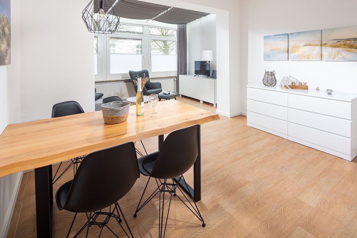 A modern dining area with a wooden table, black chairs, and a white cabinet with artwork.