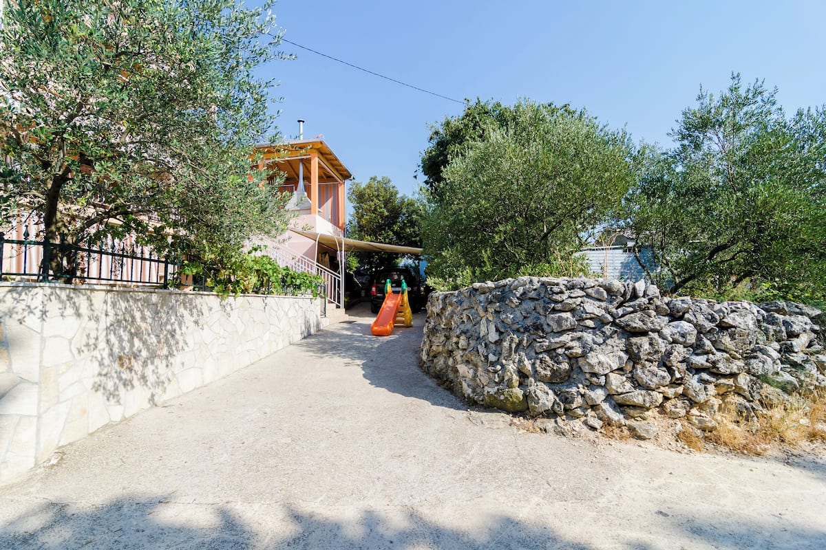 A playground with a slide and climbing structure, surrounded by trees and a stone wall.