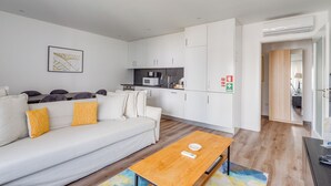 A modern living room with a sofa, a coffee table, and a kitchen area with cabinets and appliances. - Savory White Apartment, Wifi, AC !new! (Lisboa)