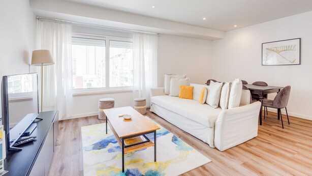 A modern living room with a white sofa, a wooden coffee table, a TV, and a dining area with a table and chairs. - Savory White Apartment, Wifi, AC !new! (Lisboa)