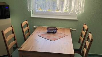 Ein Essbereich mit einem Holztisch, vier Stühlen, einem Korb und einem Fenster mit Spitzenvorhängen.