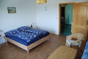 Une chambre à coucher avec un lit en bois, une petite table de chevet, une chaise en osier et une porte en bois donnant sur une autre pièce.