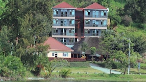 A multi-story hotel with balconies, located near a body of water and surrounded by greenery. - Delta Resort Hotel (Bwishyura)