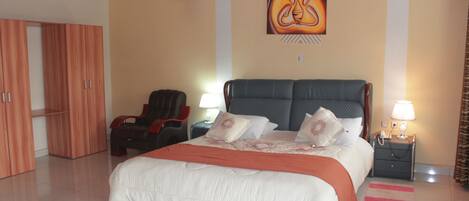 A hotel room with a large bed, a massage chair, a wardrobe, and a painting on the wall.