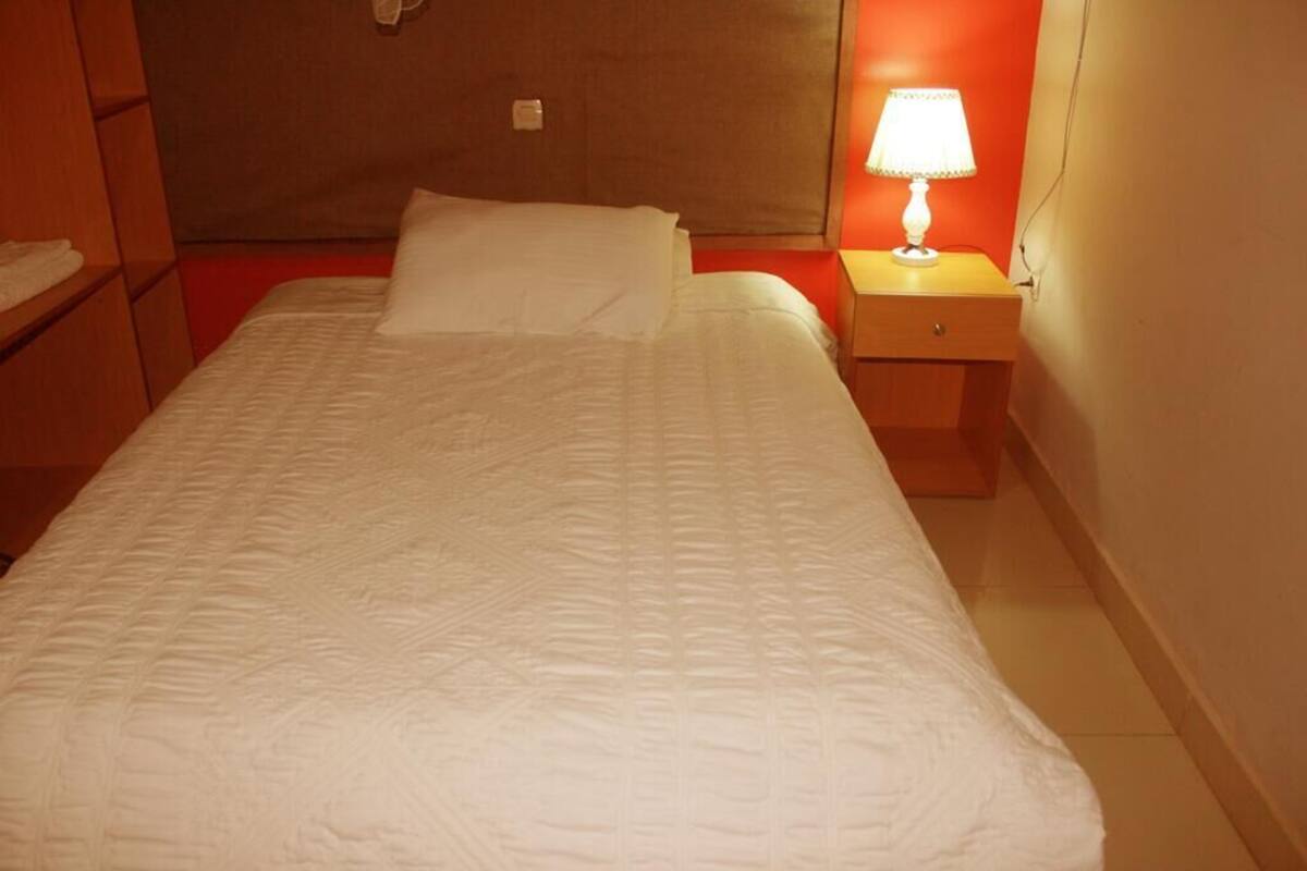 Un llit ben fet amb un edredó blanc, una làmpada de nit i una tauleta de nit de fusta.