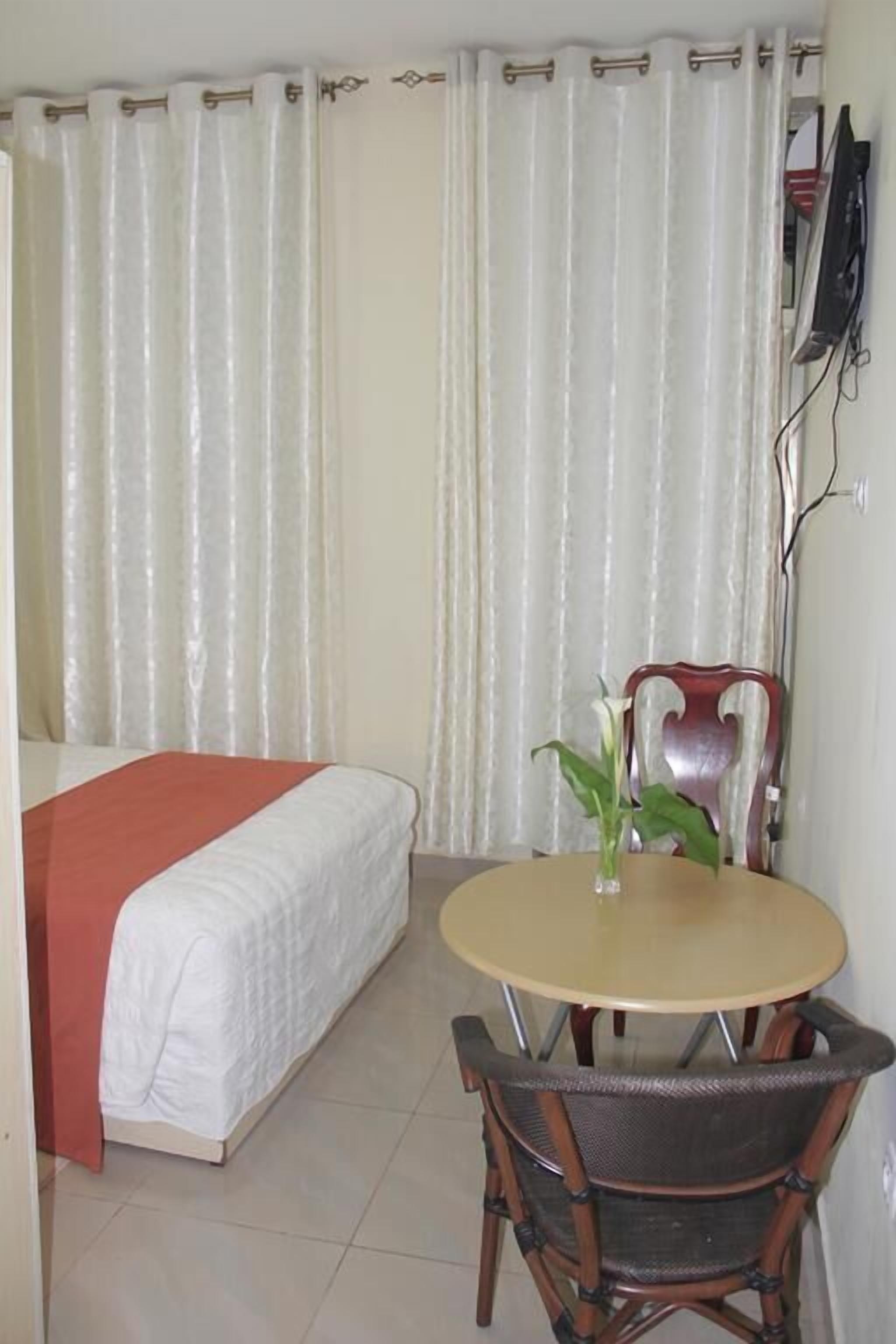 A bedroom with a bed, a small round table with a chair, and a TV mounted on the wall.