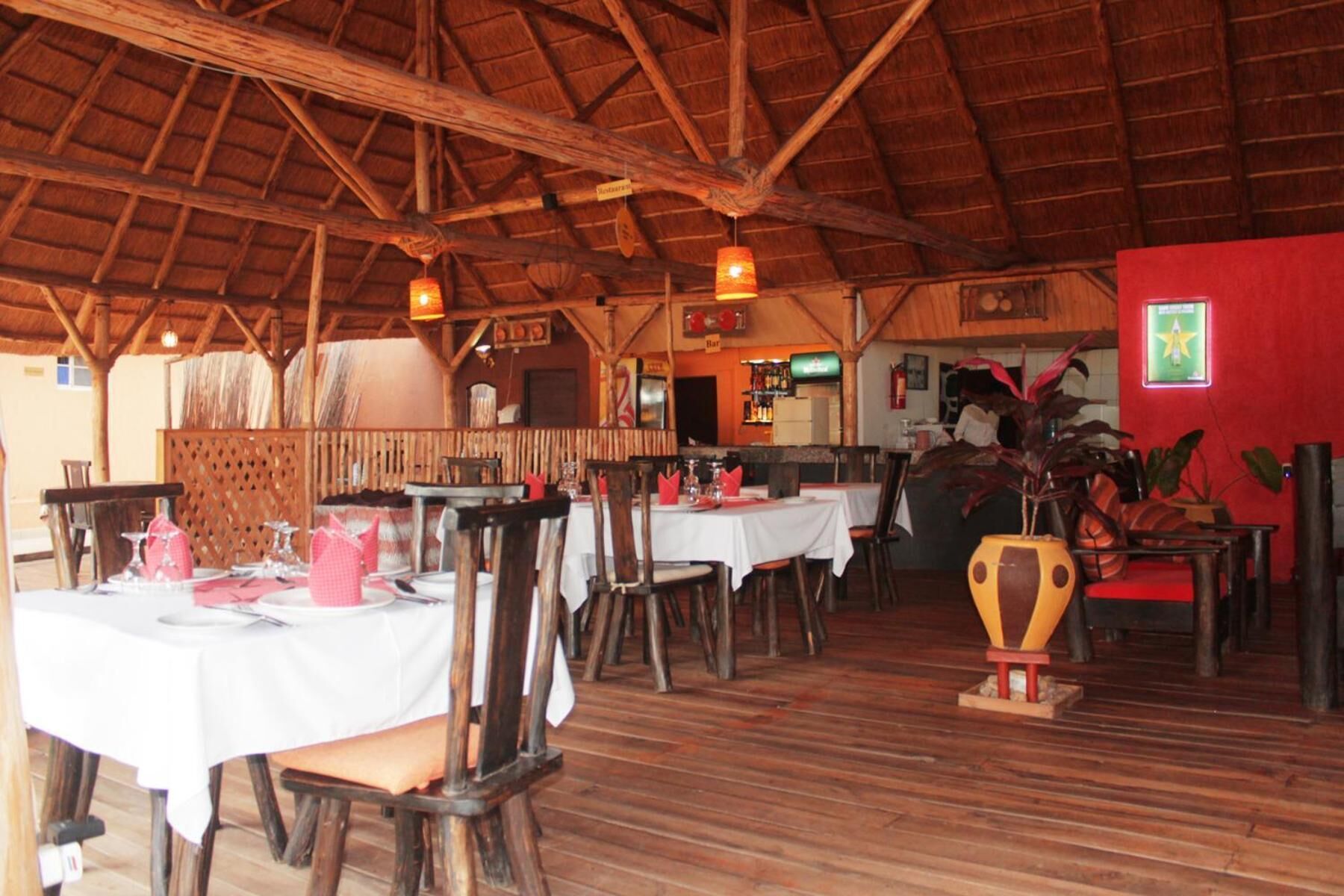 Een eetzalen met houten tafels en stoelen, een bar in de achtergrond, en een rieten dakconstructie.
