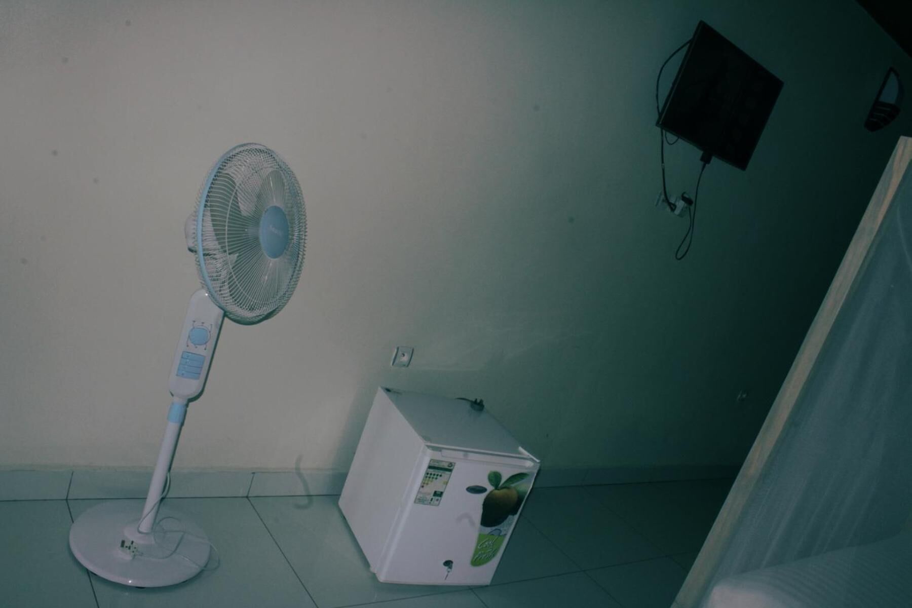 A room with a standing fan, a white appliance, and a power outlet on the wall.