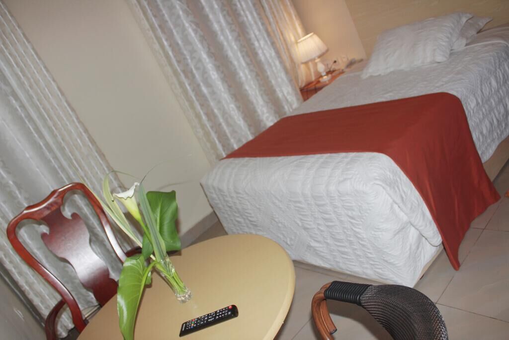 A hotel room with a bed, a chair, a small table, and a remote control.