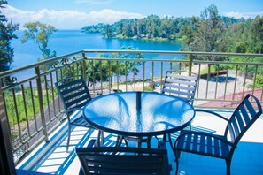 Un balcón con una mesa redonda de vidrio y cuatro sillas, con vistas a un lago y zona boscosa.