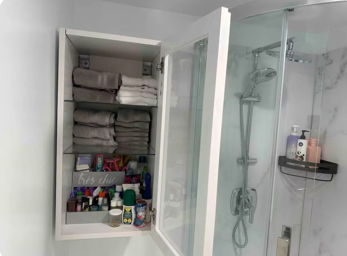 A bathroom with a glass-enclosed shower, a shelf with toiletries, and neatly folded towels.