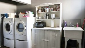 Un espace buanderie comprenant deux machines à laver à chargement frontal, un meuble avec des étagères au-dessus et une petite table avec un évier.