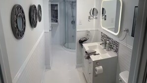 Une salle de bain moderne avec une douche à l’italienne, un meuble-lavabo avec un miroir et des toilettes.