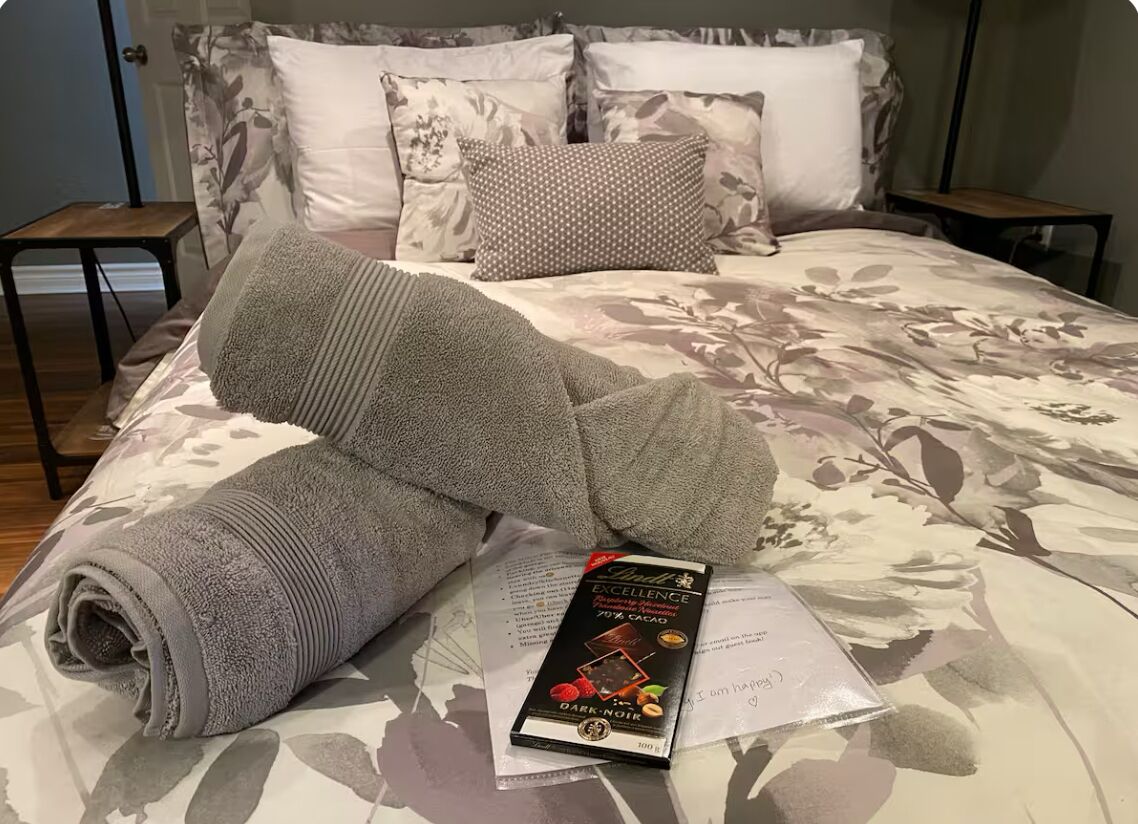 A neatly made bed with a floral bedspread, a rolled gray towel, and a book titled "Andel Excellence" on the bed.