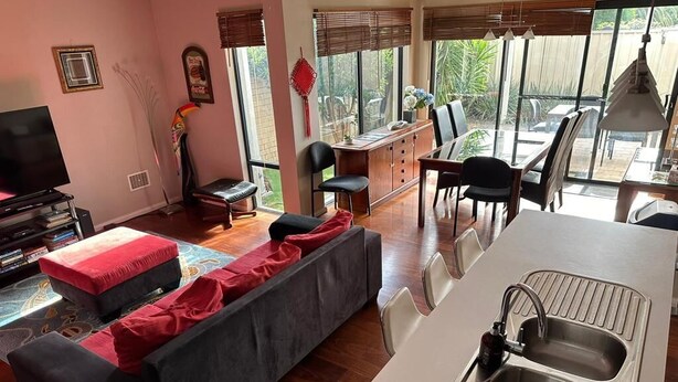 A living room with a sofa, a TV, and a dining area with chairs and a table. - Modern Melville Plaza Townhouse close to Swan River and Port beach. (Palmyra)