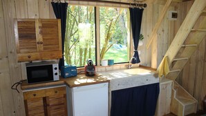 Een compacte keuken met houten kastjes, een magnetron, een kleine koelkast en een raam met gordijnen.