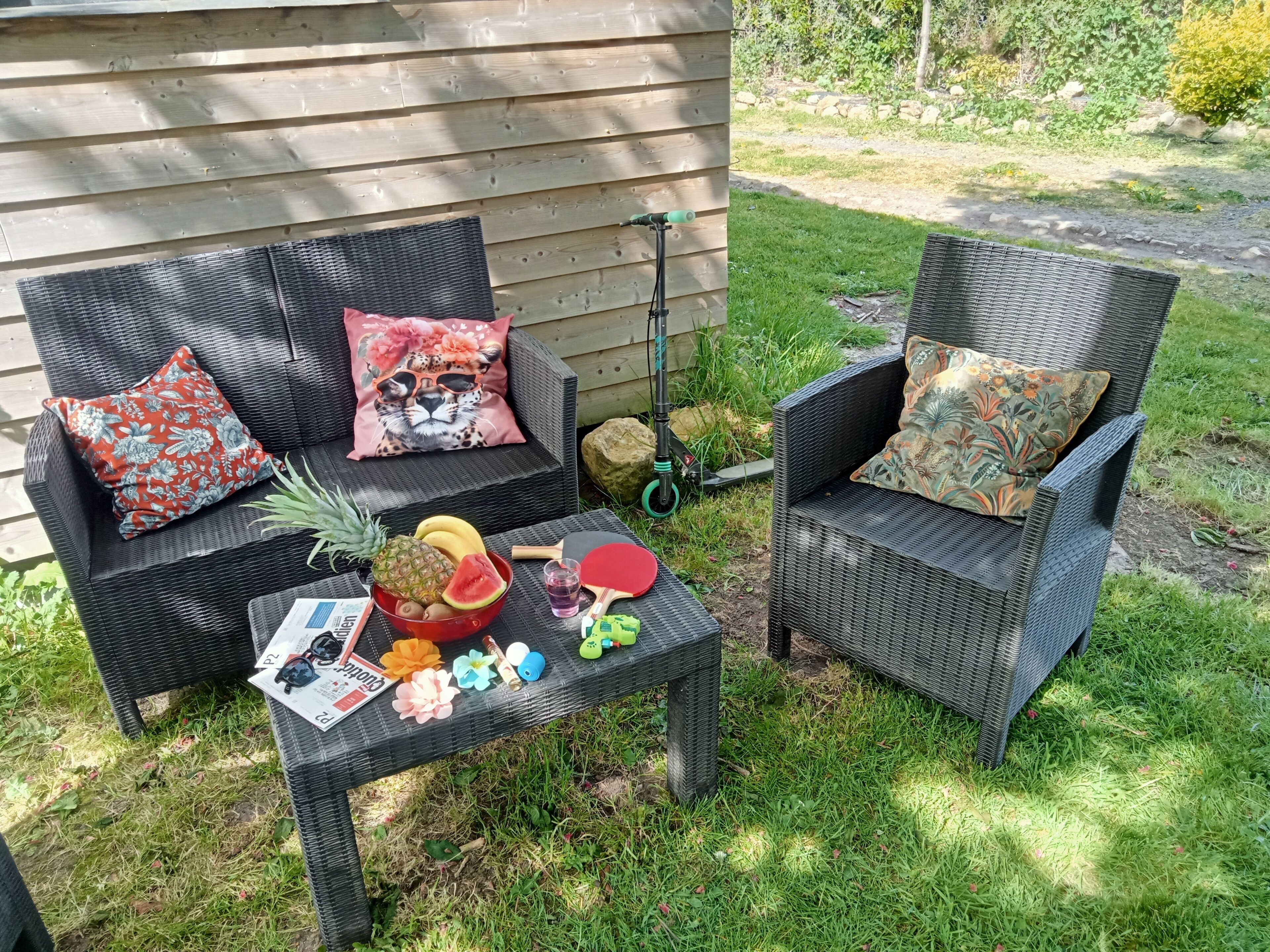 Zwei Korbstühle mit floralen Kissen, ein Tisch mit Früchten, einem Getränk und einem Roller.