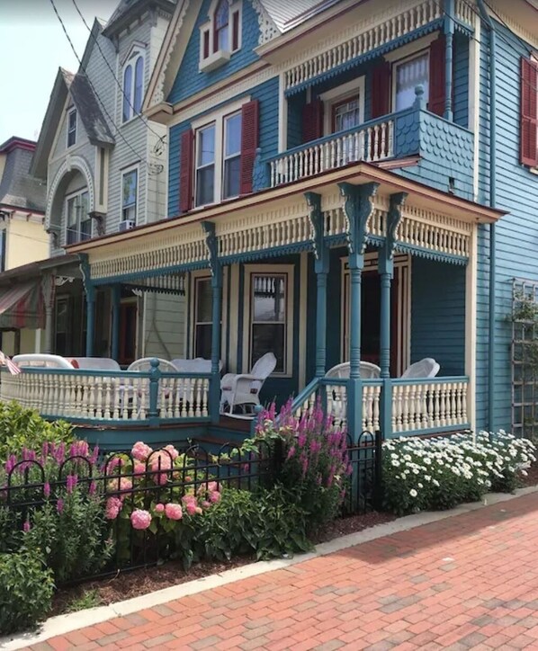 A two-story Victorian-style house with a porch, white chairs, and a brick pathway. - Beautiful 6 BR House in center of  Historic District 1 Block to Beach   (Cape May)