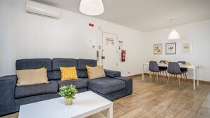 Un salon moderne avec un canapé gris, une table basse blanche et un coin repas comprenant une table blanche et des chaises grises.