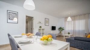 Un salon moderne avec une table à manger dressée pour deux personnes, un canapé gris et un téléviseur en arrière-plan.