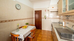A small kitchen with a dining table, chairs, a clock, and a sink.