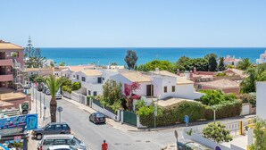 Une rue côtière bordée de bâtiments blancs, avec un ciel bleu et la mer en arrière-plan.