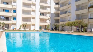 Une piscine à l’eau d’un bleu cristallin, entourée d’un immeuble à plusieurs étages doté de balcons et d’espaces de détente en plein air.