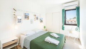 Een schone, goed verlichte slaapkamer met een bed, nachtkastje, stoel en een raam met gordijnen.