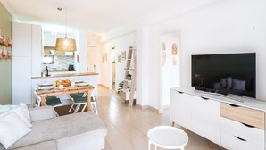 Een moderne woonkamer met een bank, een eettafel en een televisie op een wit kastje.