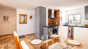 Een moderne keuken met een eetgedeelte, met een glazen tafel, grijze kasten en een houten vloer.