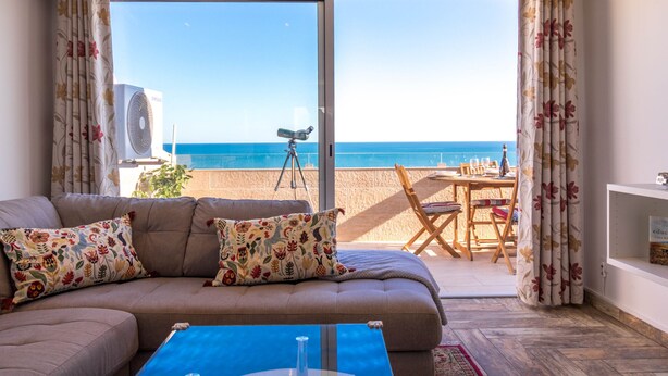 Een woonkamer met een bank, een salontafel en een balkon met uitzicht op zee.