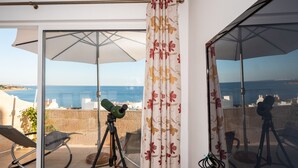 Een balkon met een telescoop, een stoel en uitzicht op zee.