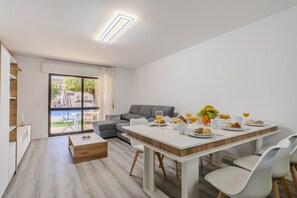 A modern living room with a dining area, a sofa, and a view of the outdoors.