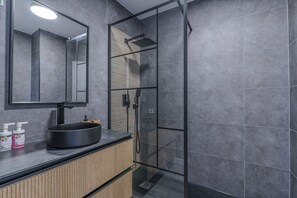 A modern bathroom with a glass shower enclosure, a round sink, and a mirror above it.