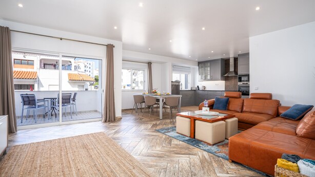 A spacious living area with a large sofa, a dining table, and a kitchen in the background. - #034 Tebay by Home Holidays (Albufeira)