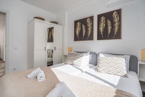 Een slaapkamer met een bed, kussens, een garderobe en twee bladkunstwerken in lijsten aan de muur.