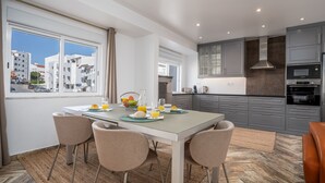 A modern kitchen with grey cabinets, a stainless steel range hood, and a dining area with a table set for two. - #034 Tebay by Home Holidays (Albufeira)