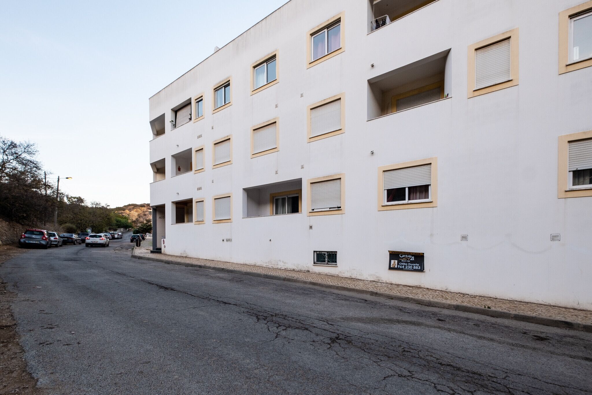 A multi-story building with a white facade and yellow window frames. There are several cars parked along the street in front.