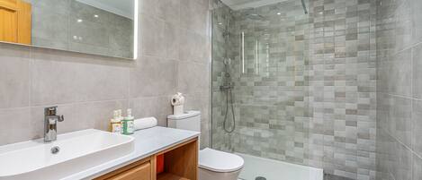 A modern bathroom with a glass-enclosed shower, a white sink, and a wooden vanity.