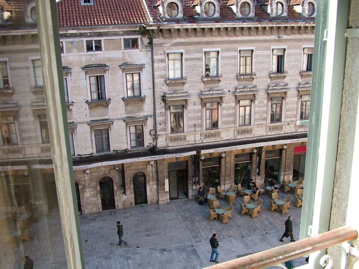 A courtyard with outdoor seating, stone buildings, and a view of the street.