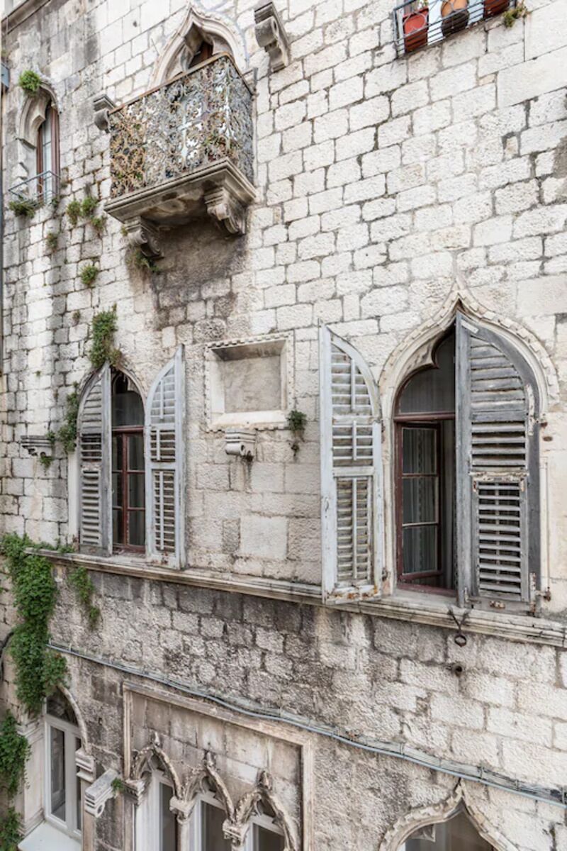 A historic building with arched windows, a balcony with ornate metalwork, and stone walls.