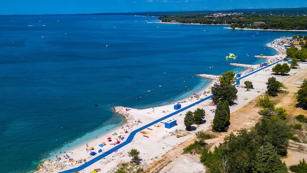 An aerial view of a coastal beach with clear blue waters, a sandy shore, and a blue pathway along the beach. - Villa Elena Deluxe with whirlpool and POOL by the SEA (Fažana)