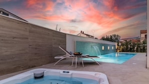 A modern outdoor pool area with a hot tub, lounge chairs, and a view of the sunset. - Villa Elena Deluxe with whirlpool and POOL by the SEA (Fažana)