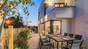 A modern outdoor dining area with a table set for four, surrounded by chairs, and a view of a two-story building with large windows. - Villa Elena Deluxe with whirlpool and POOL by the SEA (Fažana)