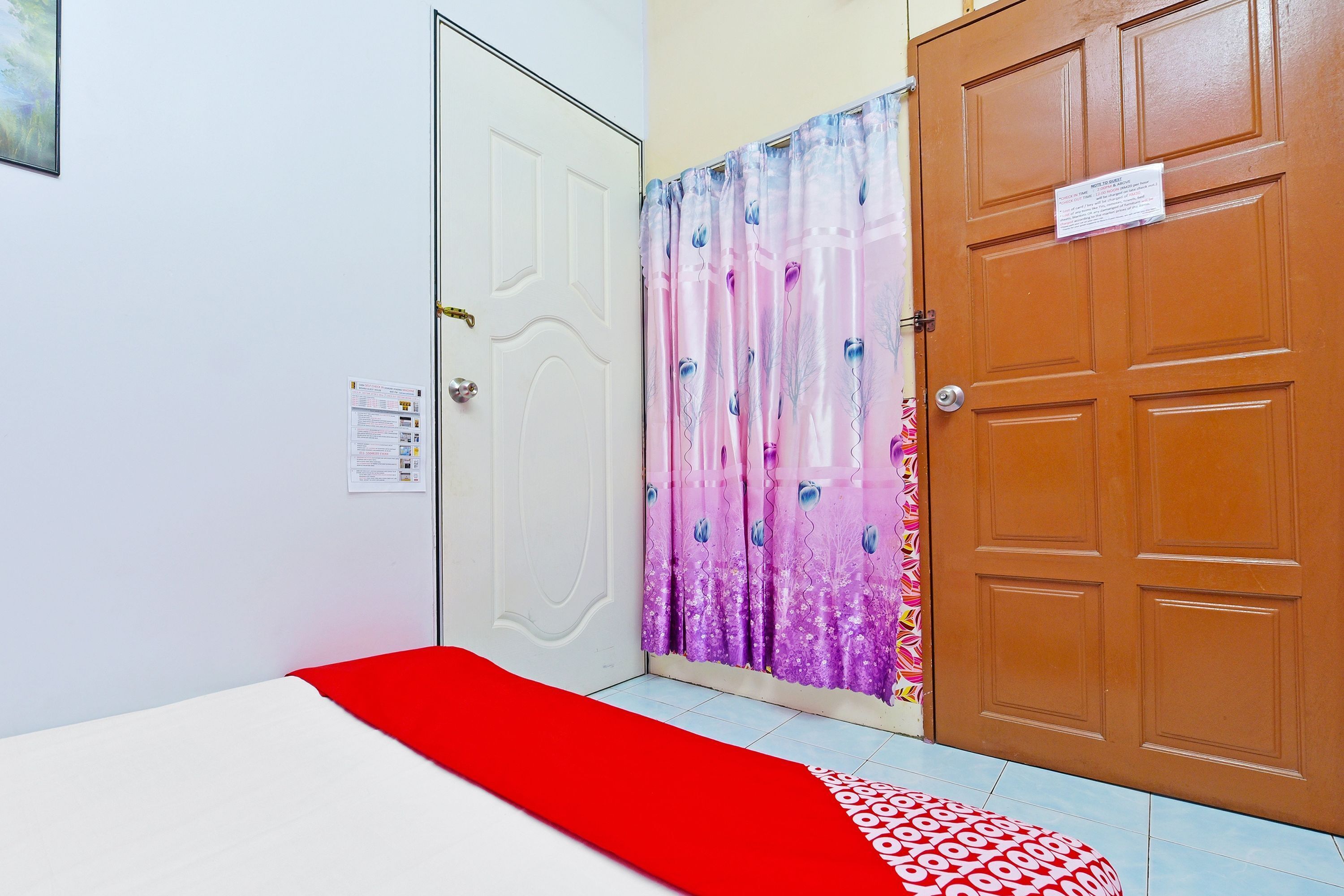 A room with a bed, a white door, a wooden door, and a curtain with a pattern.