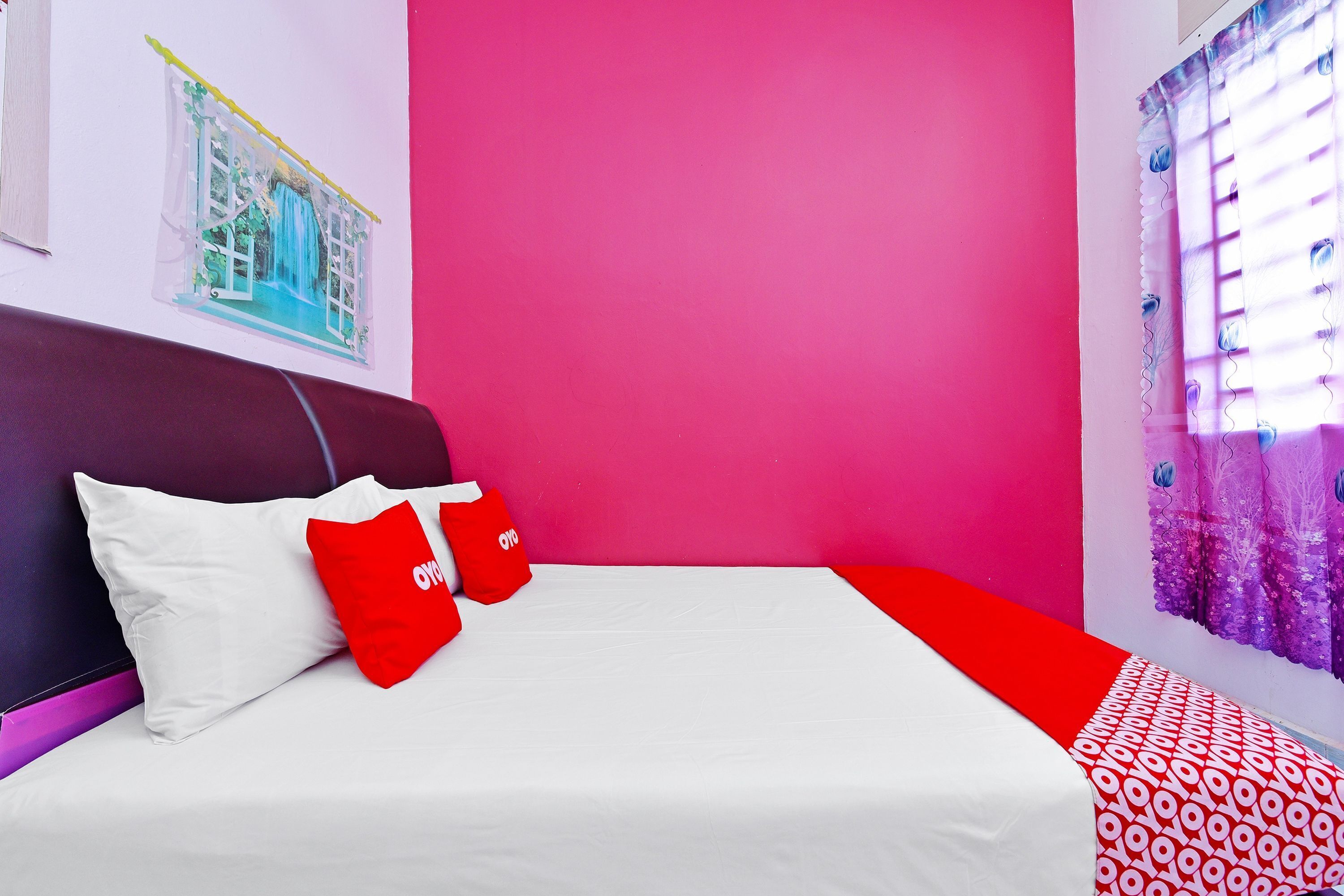 A bed with white and red bedding, a purple headboard, and a pink wall.