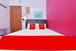 Un dormitorio con una cama, una puerta, una mesita pequeña, una lámpara de pared y una imagen de un jardín.
